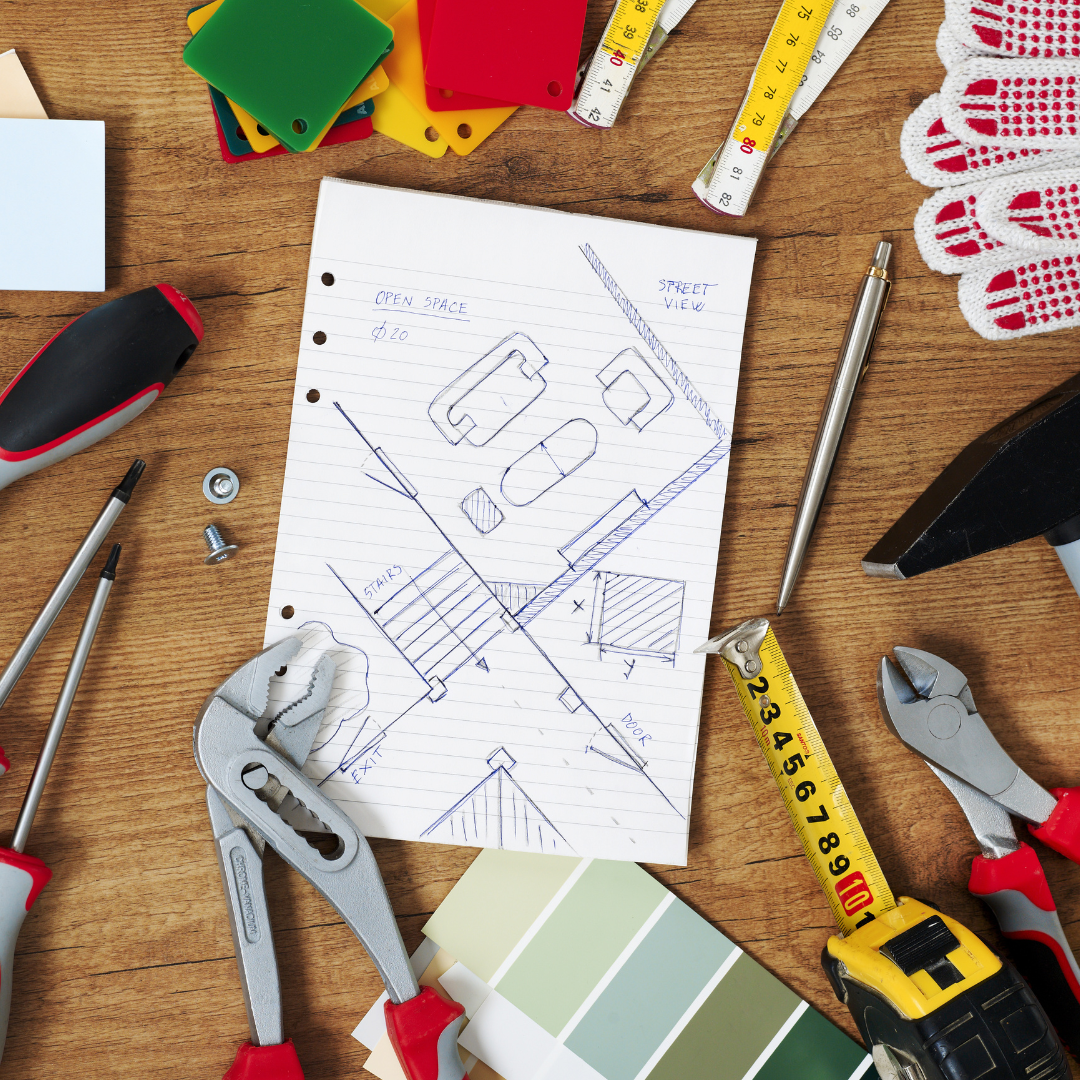 Sketch of a plan with tools, paint samples, and measuring tape on a wooden surface.