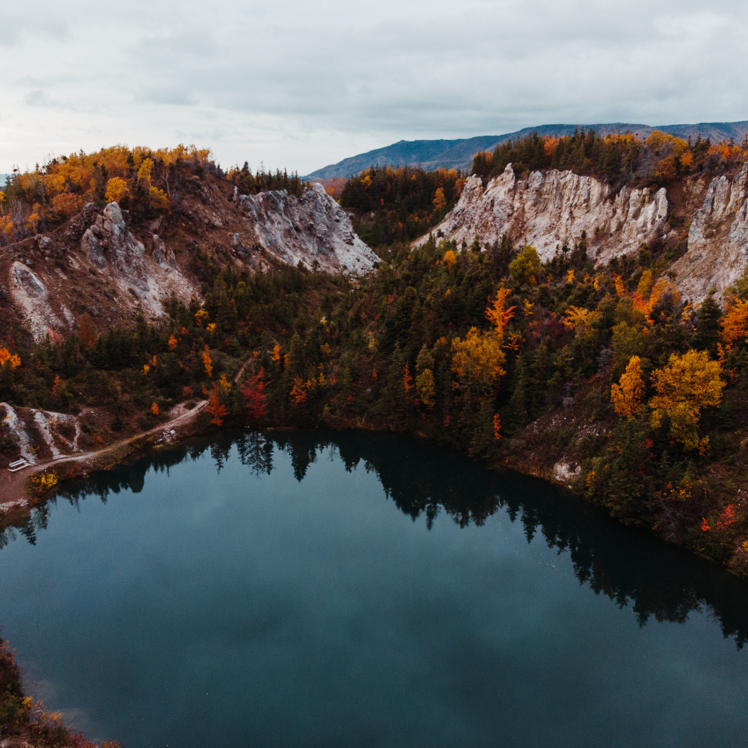A serene lake surrounded by autumn-colored trees and rugged hills, under a cloudy sky.