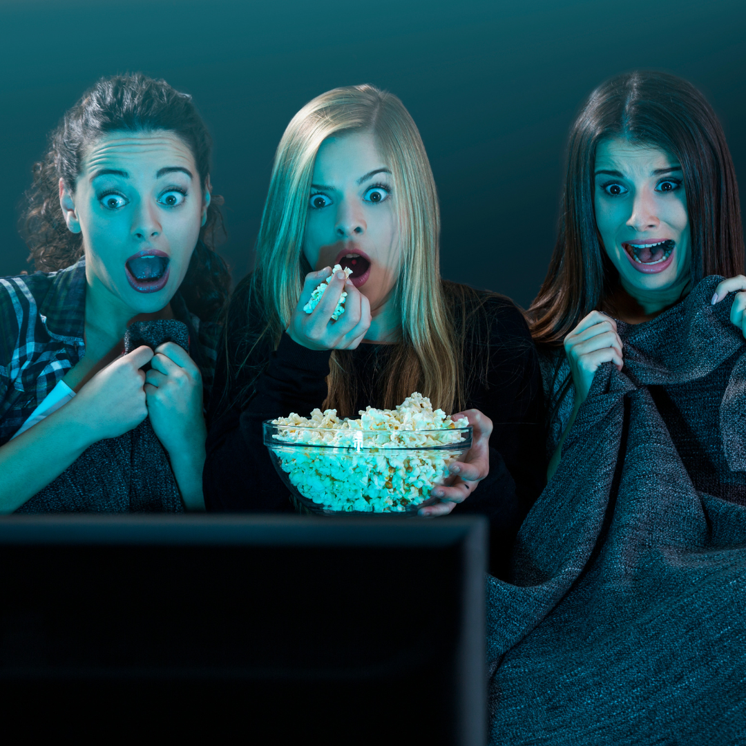 Three women watching TV, looking shocked, holding popcorn.