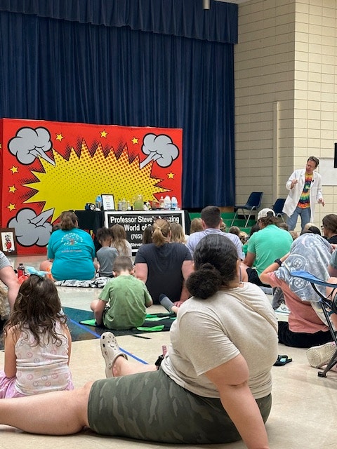 A group of people watching a person performing on a stage with a colorful comic backdrop.