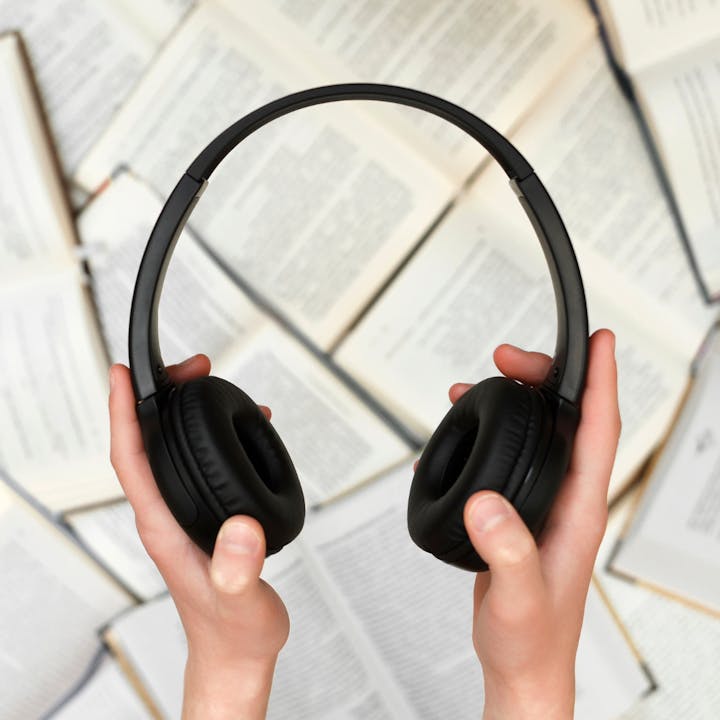 Hands holding headphones above an open book.