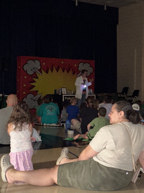 A crowd watching a performer on stage with a colorful comic-style backdrop.
