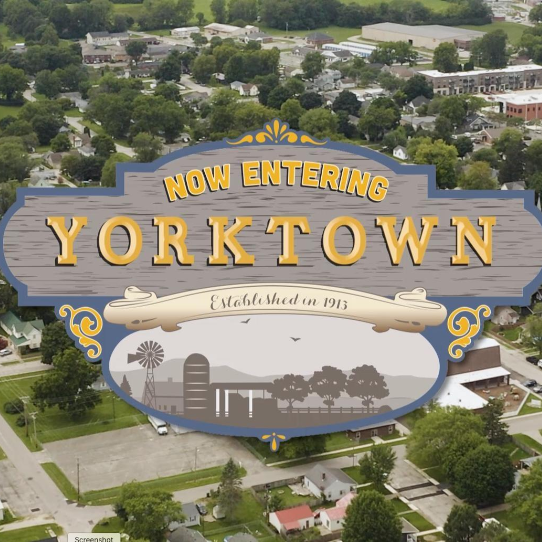 Welcome sign for Yorktown, established 1913, with a rural town aerial view.