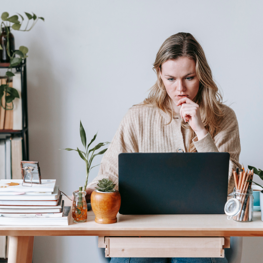 Person working on a laptop at a desk with plants, books, and stationery.