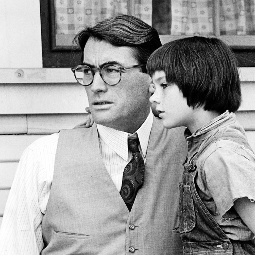 A man with glasses and a young child stand closely, looking in the same direction.