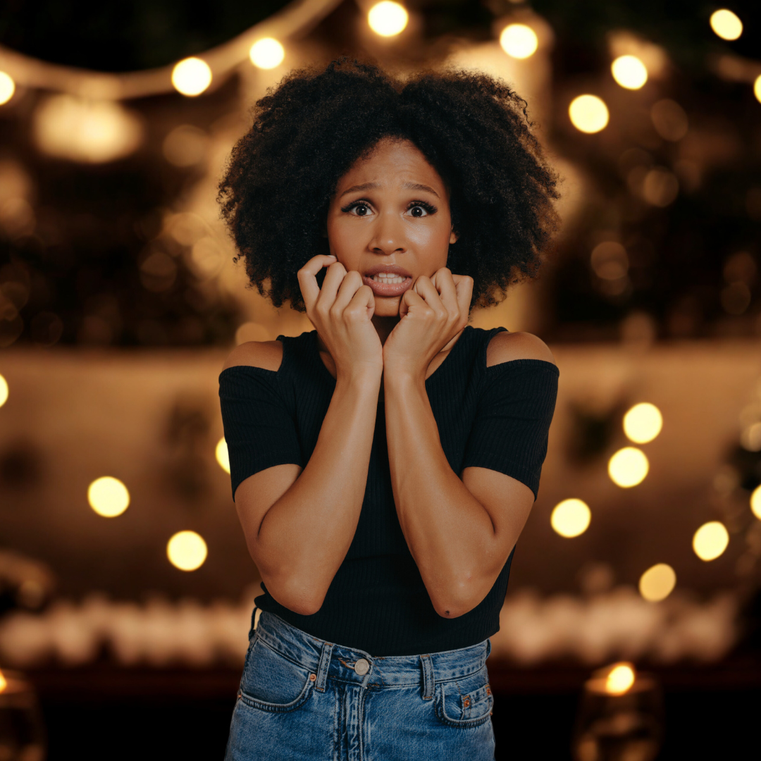 A woman with curly hair looks anxious, biting her nails and showing distress, surrounded by soft, blurred lights.