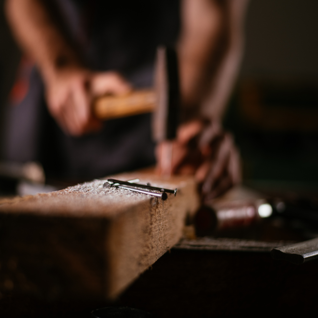 Person chiseling wood with a mallet and chisel, woodworking tools on bench, close-up, focus on wood shavings.