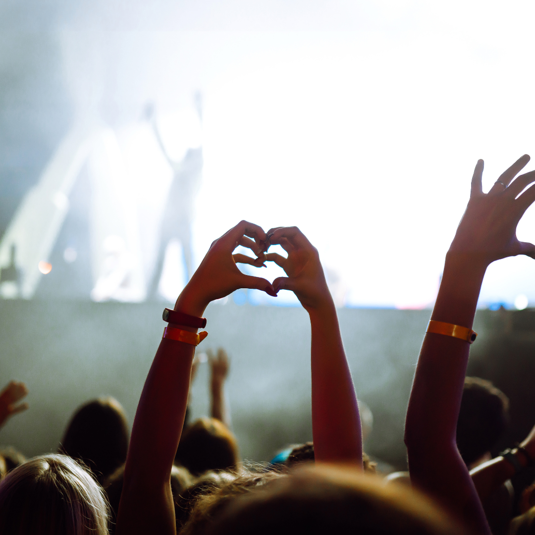 Audience at a concert with a person making a heart shape with their hands.