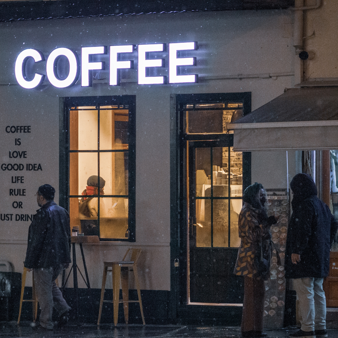 A cozy coffee shop at night with people outside in snowy weather.