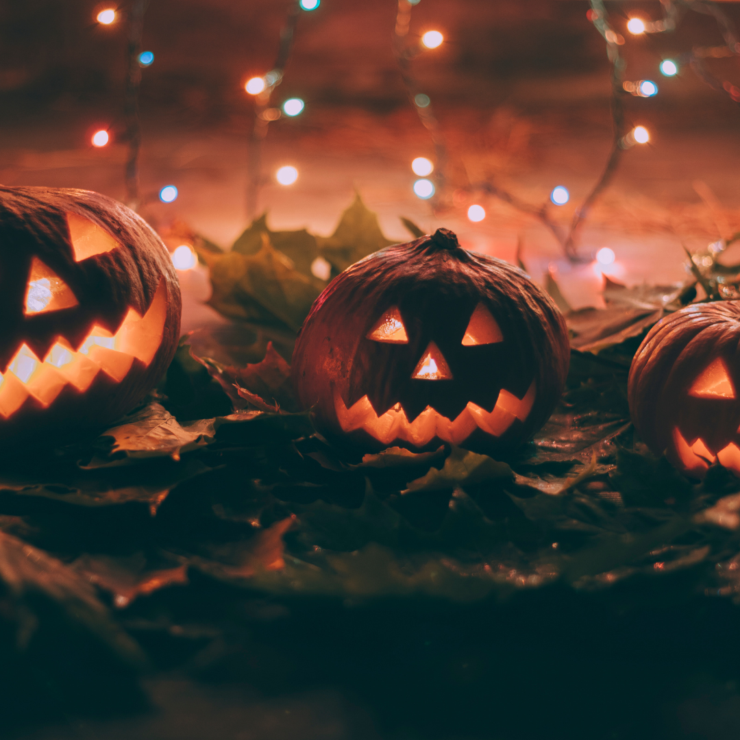 Three jack-o'-lanterns with a backdrop of twinkling lights and autumn leaves.