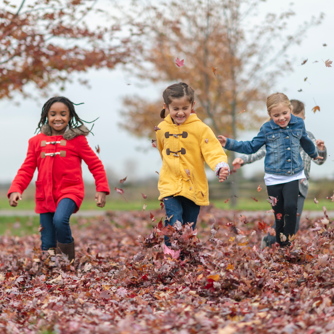 Three children playing and running through autumn leaves.