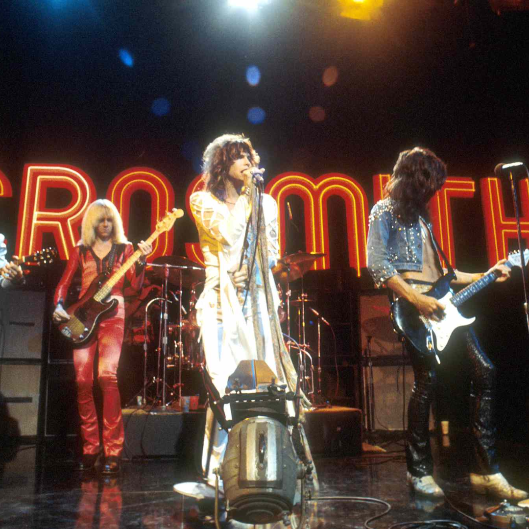 A rock band performing on stage with the band's name in lights behind them.