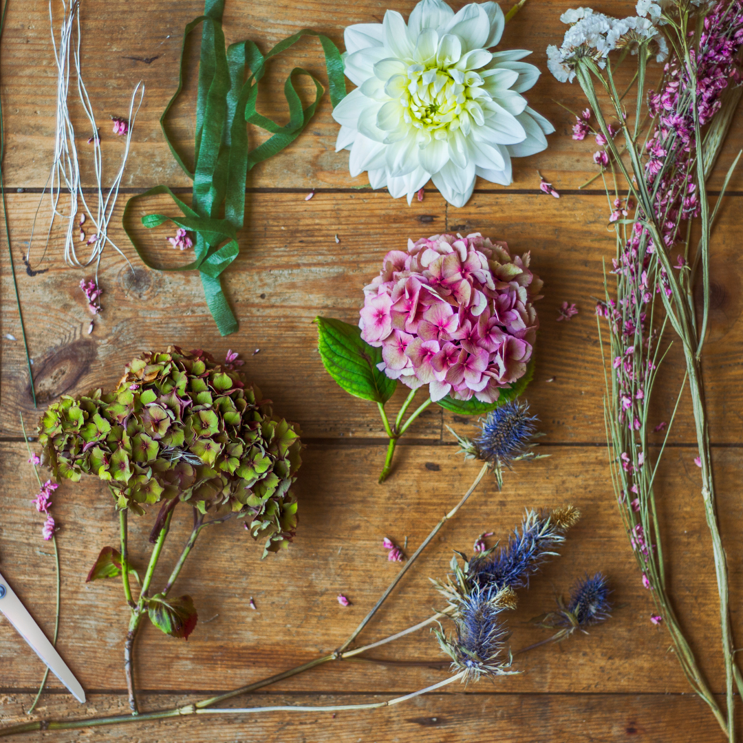 Flowers and crafting materials on a wooden surface: hydrangeas, ribbon, scissors, and dried stems.