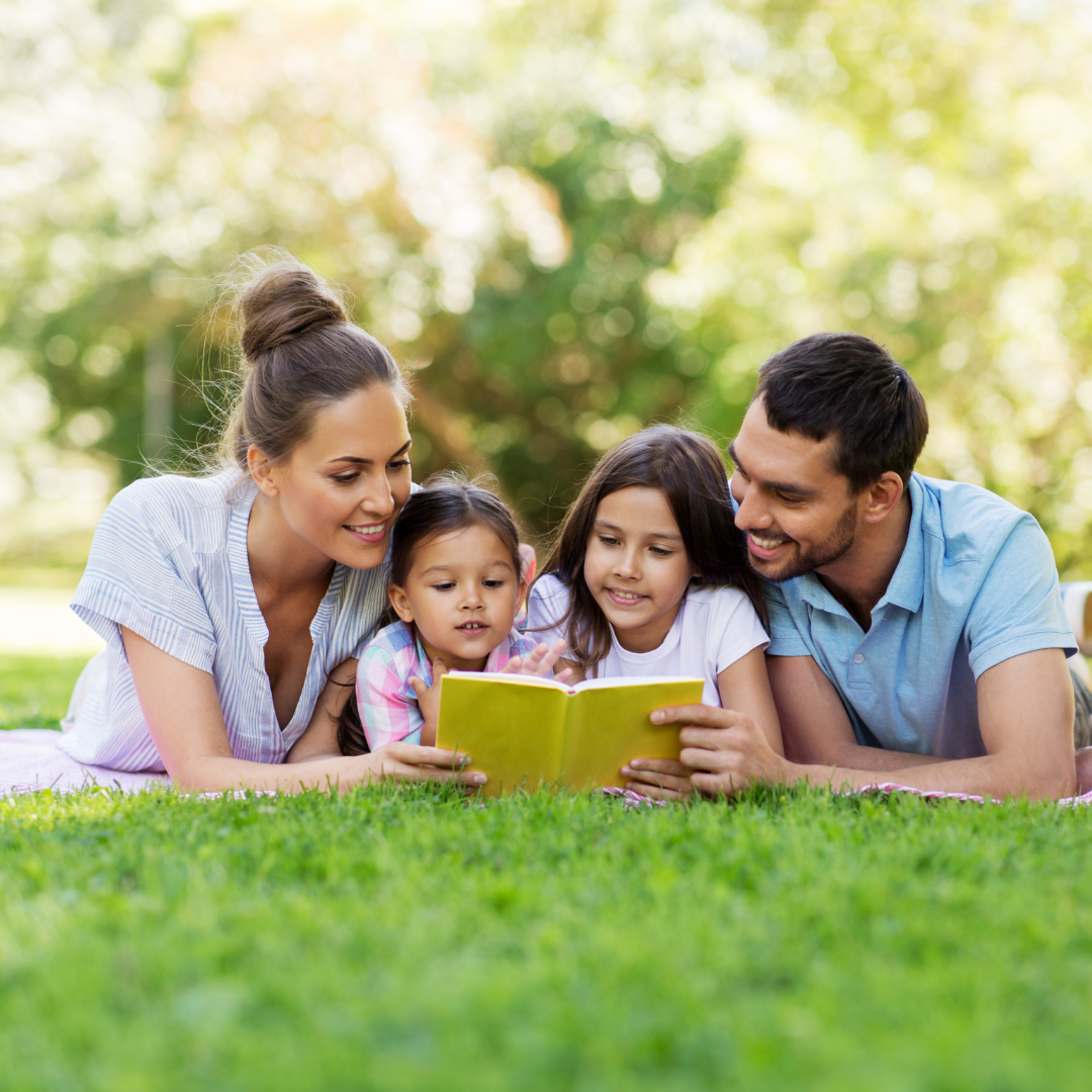 A family of four enjoying a book together outdoors.
