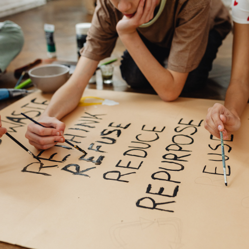 Kids are painting messages on paper, promoting sustainability with words like "Refuse," "Reduce," "Reuse," and "Repurpose."