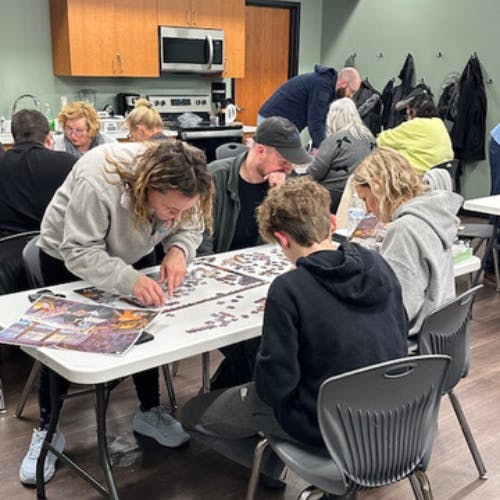 A group of people working together at tables on puzzles in a casual indoor setting.