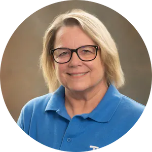 Portrait of a smiling woman with glasses wearing a blue polo shirt.