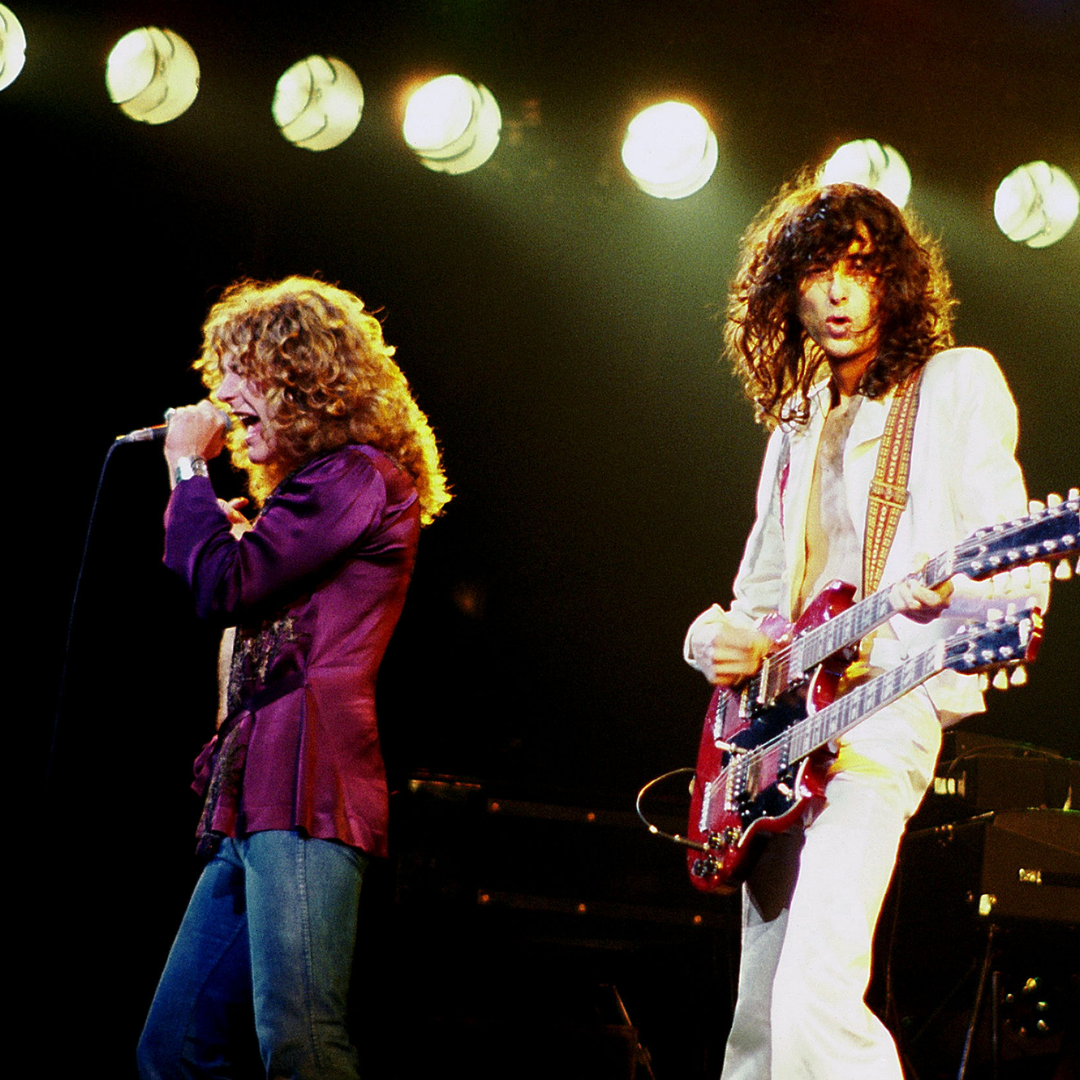 Two musicians perform on stage with bright lights behind them; one sings, the other plays a guitar.
