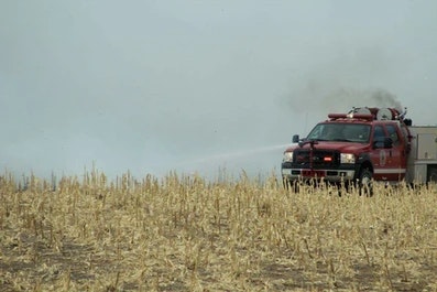 A fire truck spraying water in a dry field with smoke in the background.