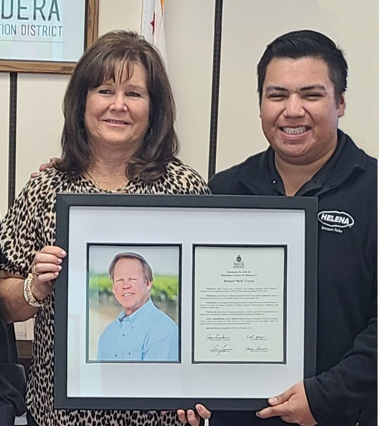 Two people smiling and holding a framed picture and certificate.