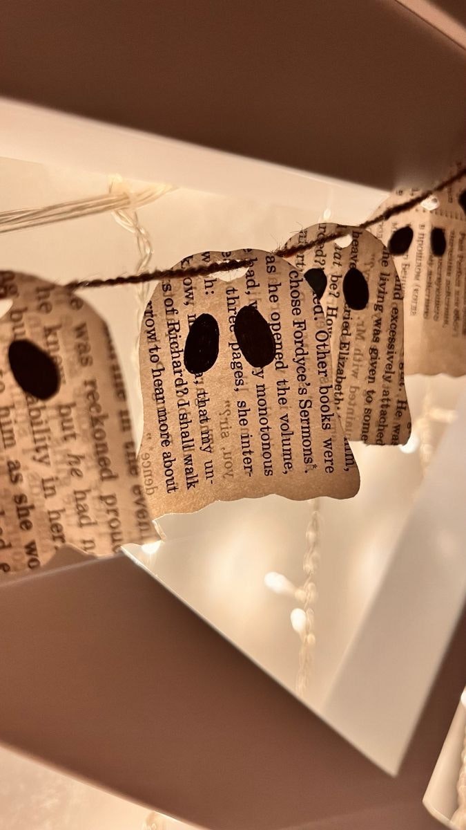 Paper ghosts with print text hanging as a garland, decorated with string lights.