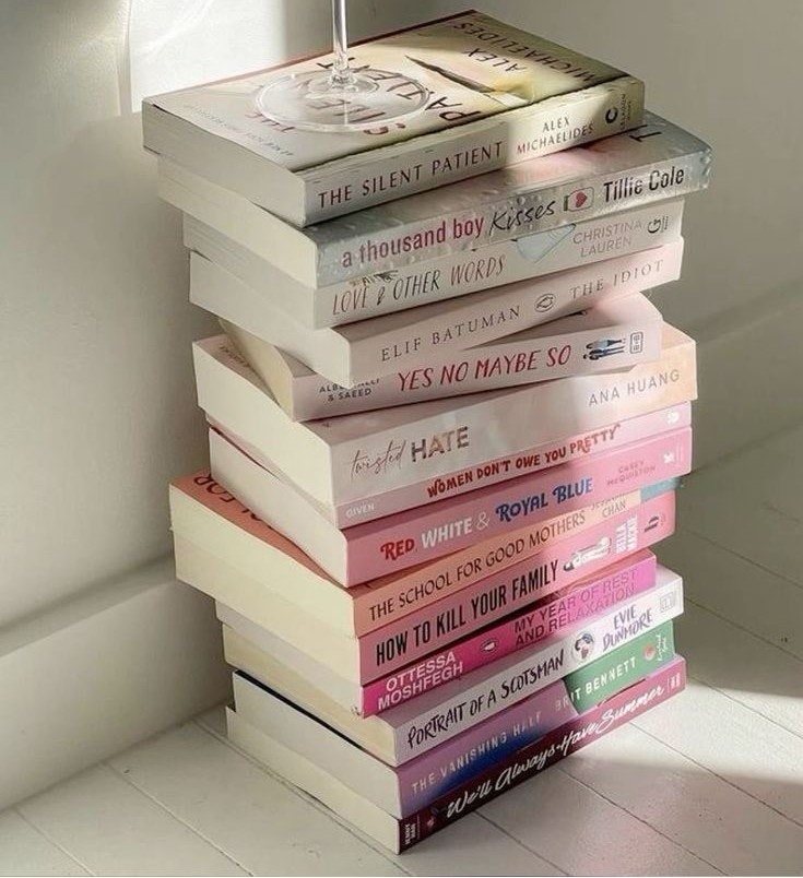 A stack of books with a wine glass balanced on top, placed in soft lighting.