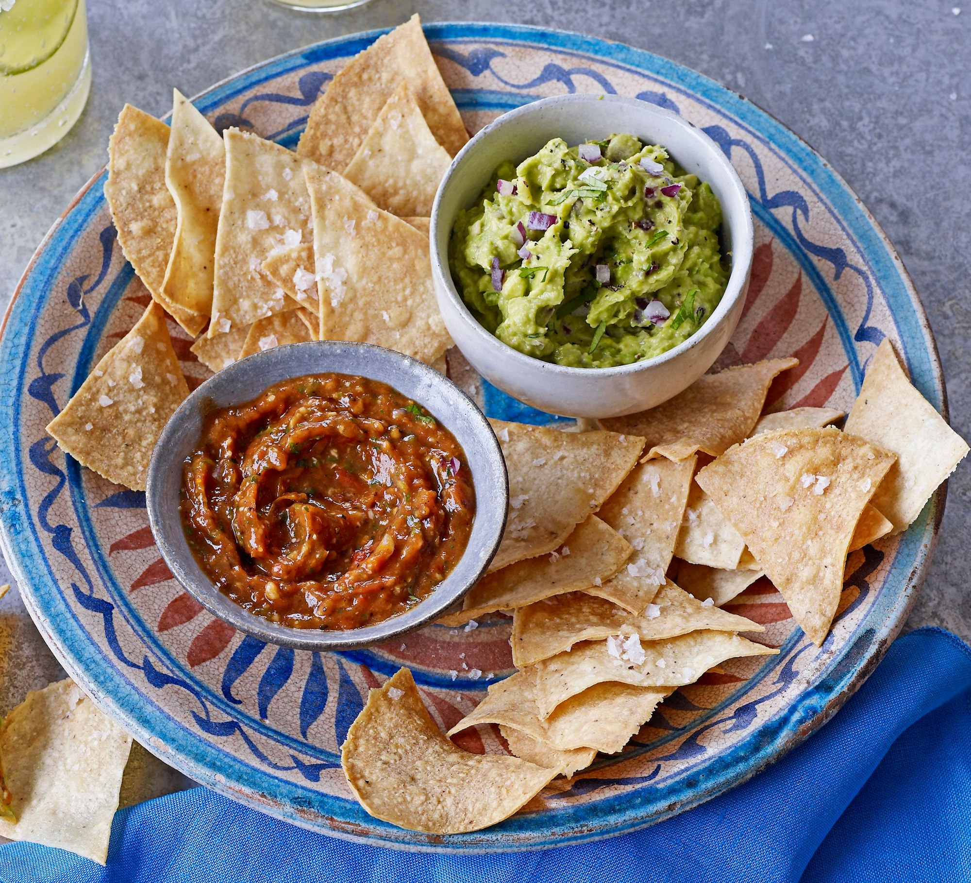 The image features a colorful plate with tortilla chips, guacamole, and salsa, ready for dipping.