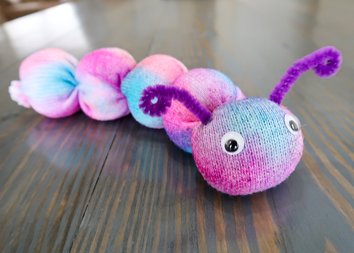 A colorful caterpillar made from socks with googly eyes and pipe cleaner antennae, placed on a wooden surface.