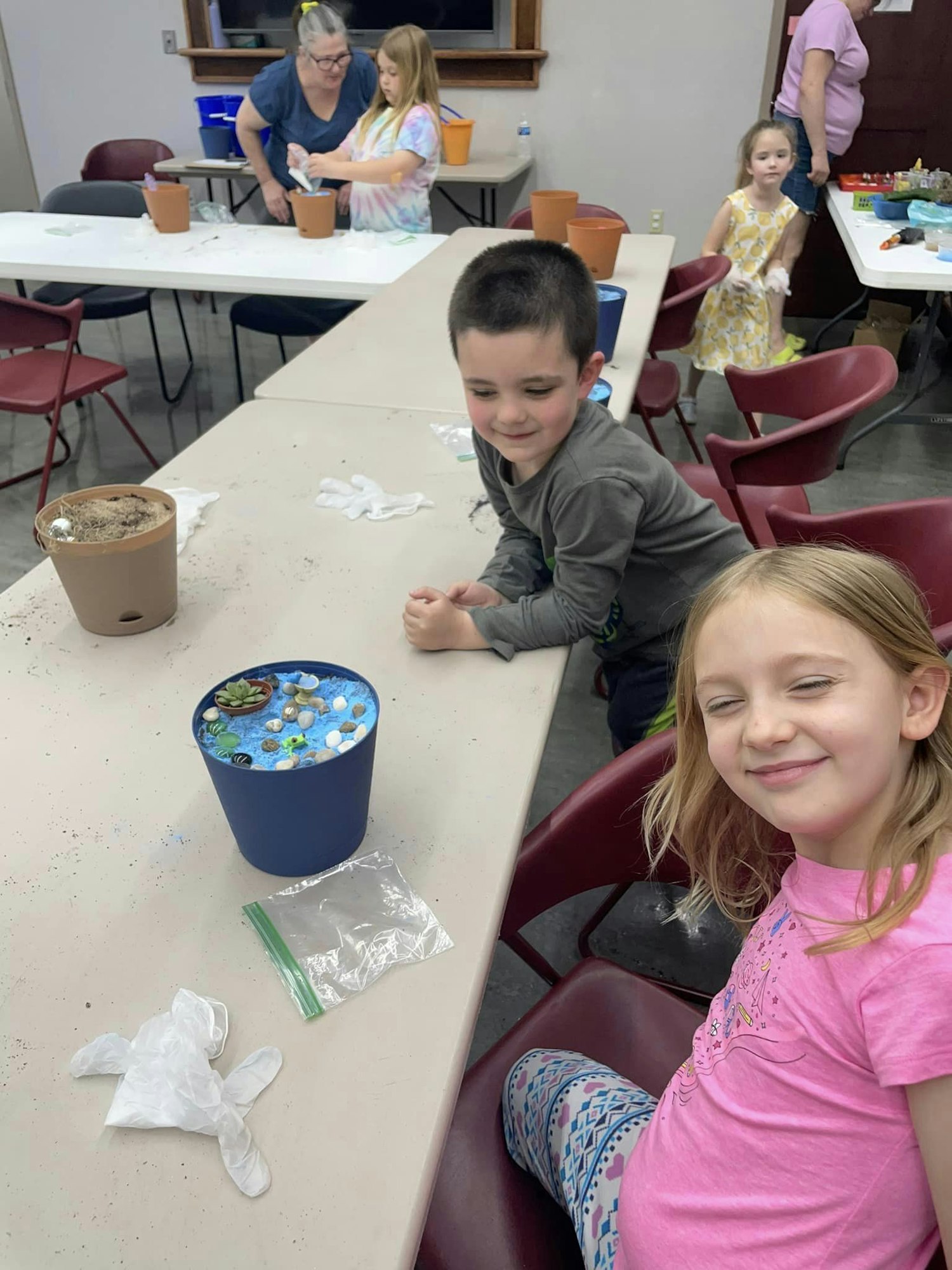 Children at a craft activity, with a decorated flowerpot on the table.