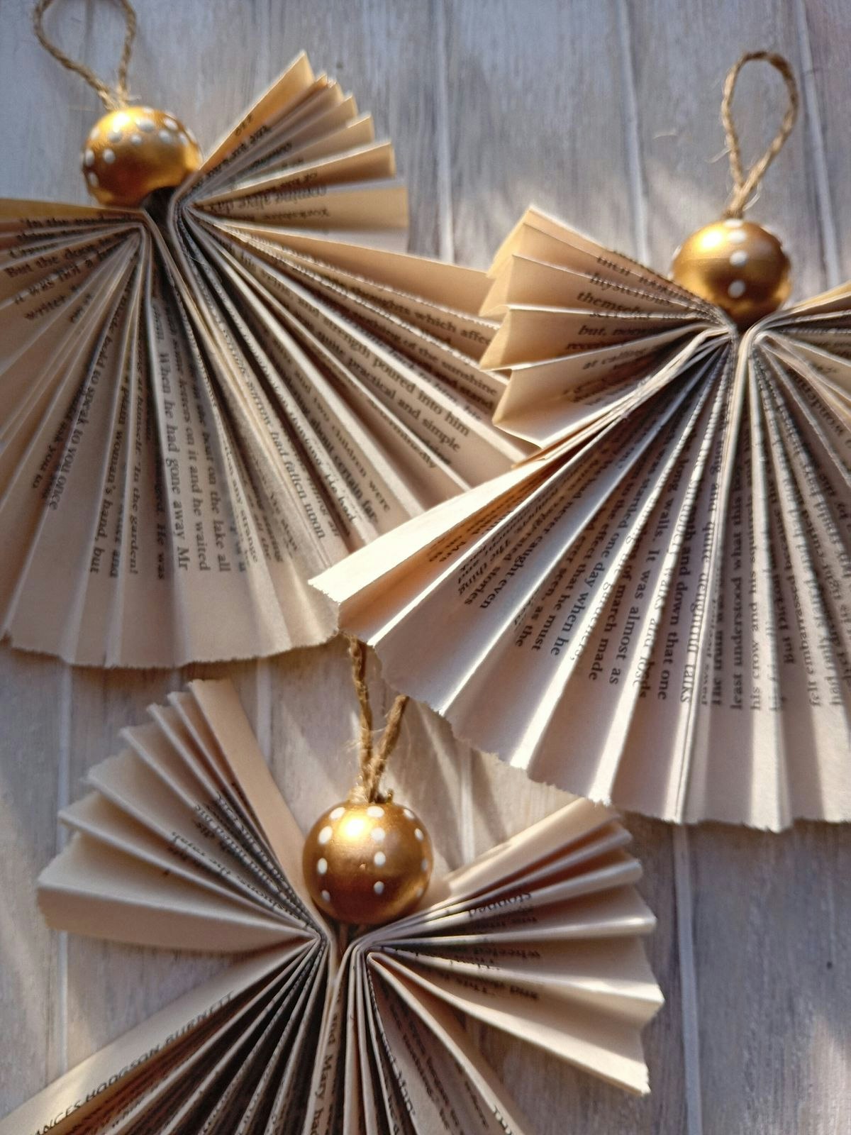 The image features decorative angels made from folded book pages, topped with gold polka-dotted spheres and twine for hanging.
