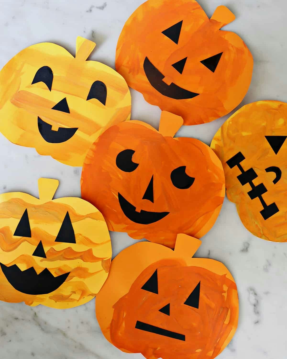 Paper pumpkins with various black cut-out faces on a marble surface.