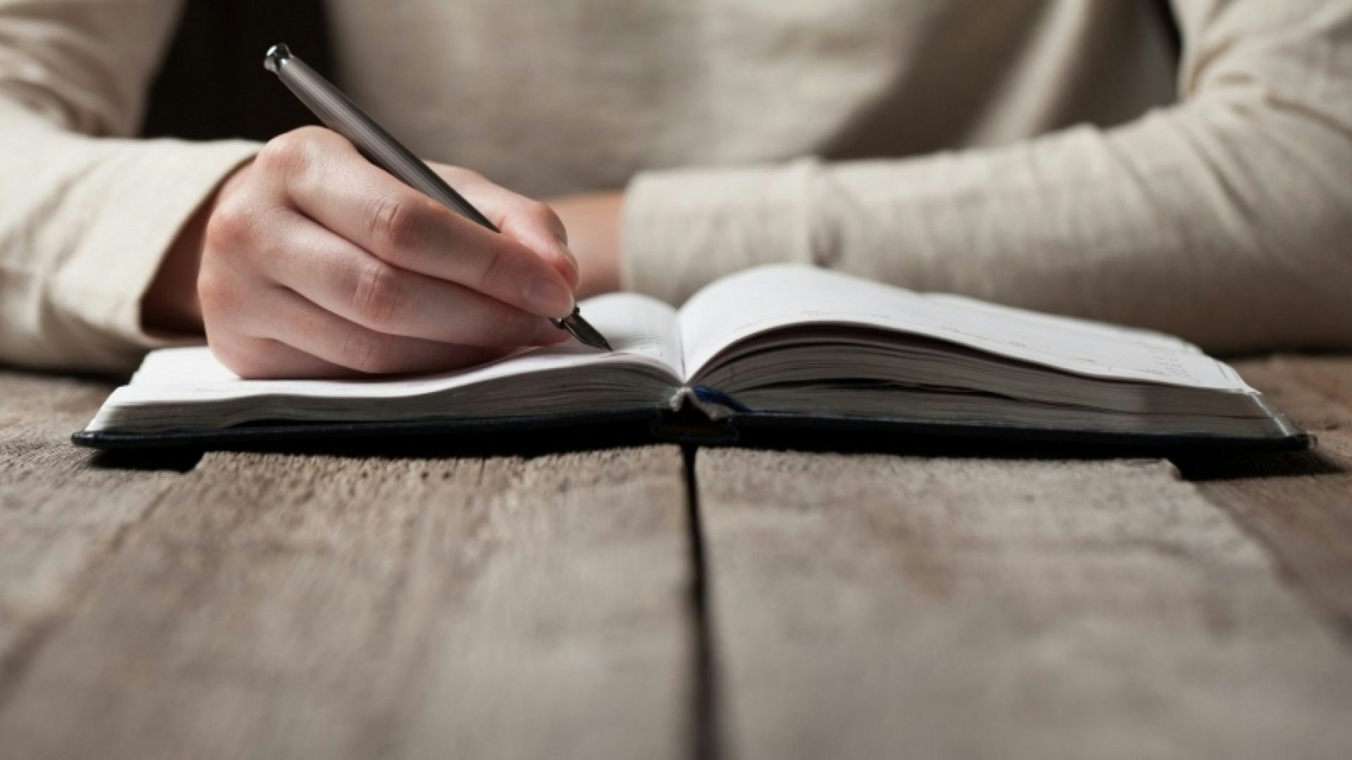 A person writes in a notebook on a wooden table.
