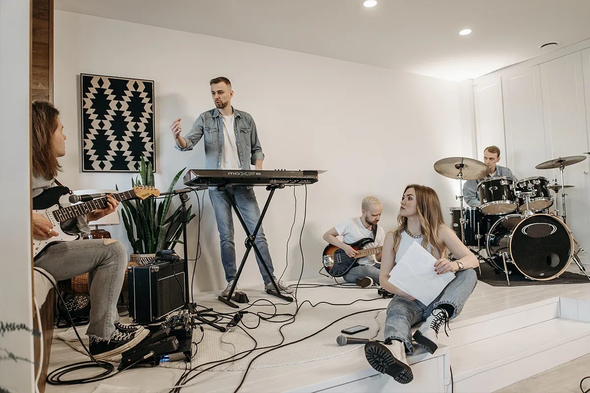 Four musicians with instruments in a band rehearsal room.