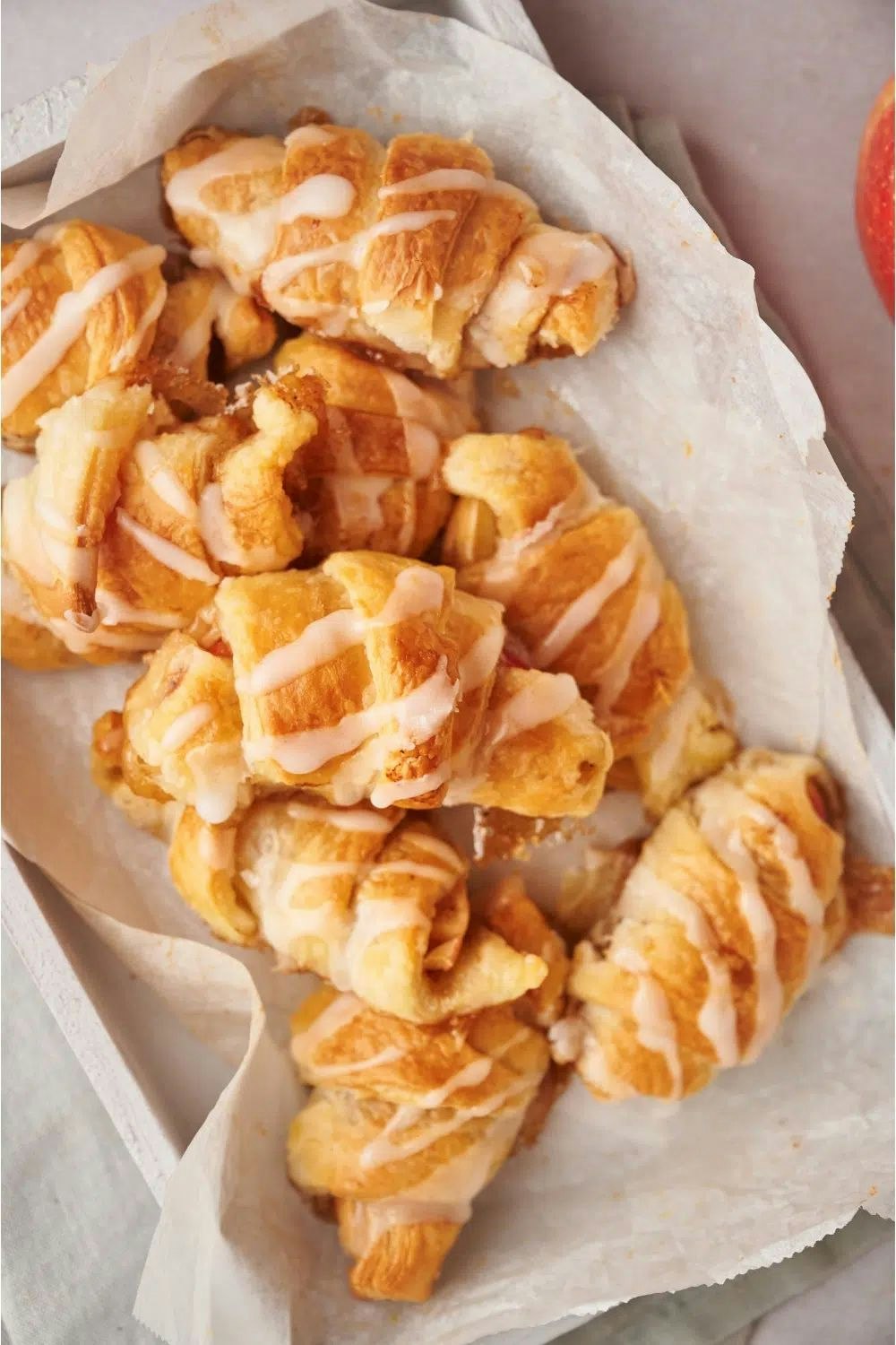 Croissants drizzled with icing on parchment paper in a tray.