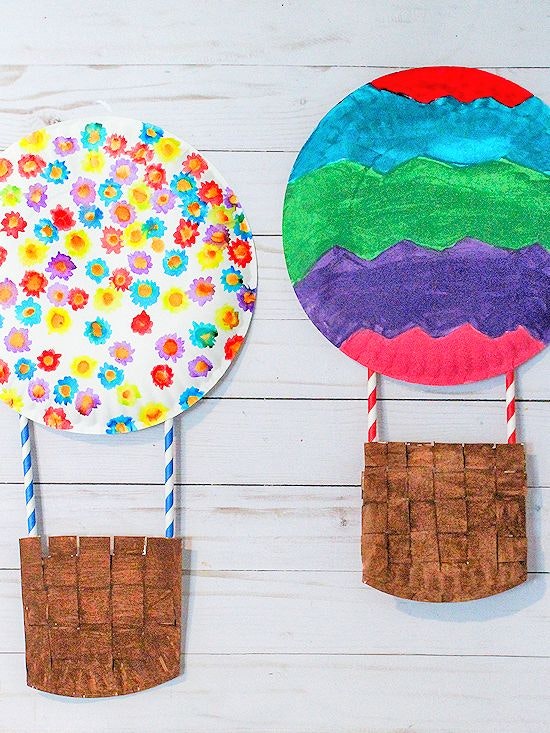Two hot air balloons made from paper plates and straws, with colorful decorations on a wooden background.