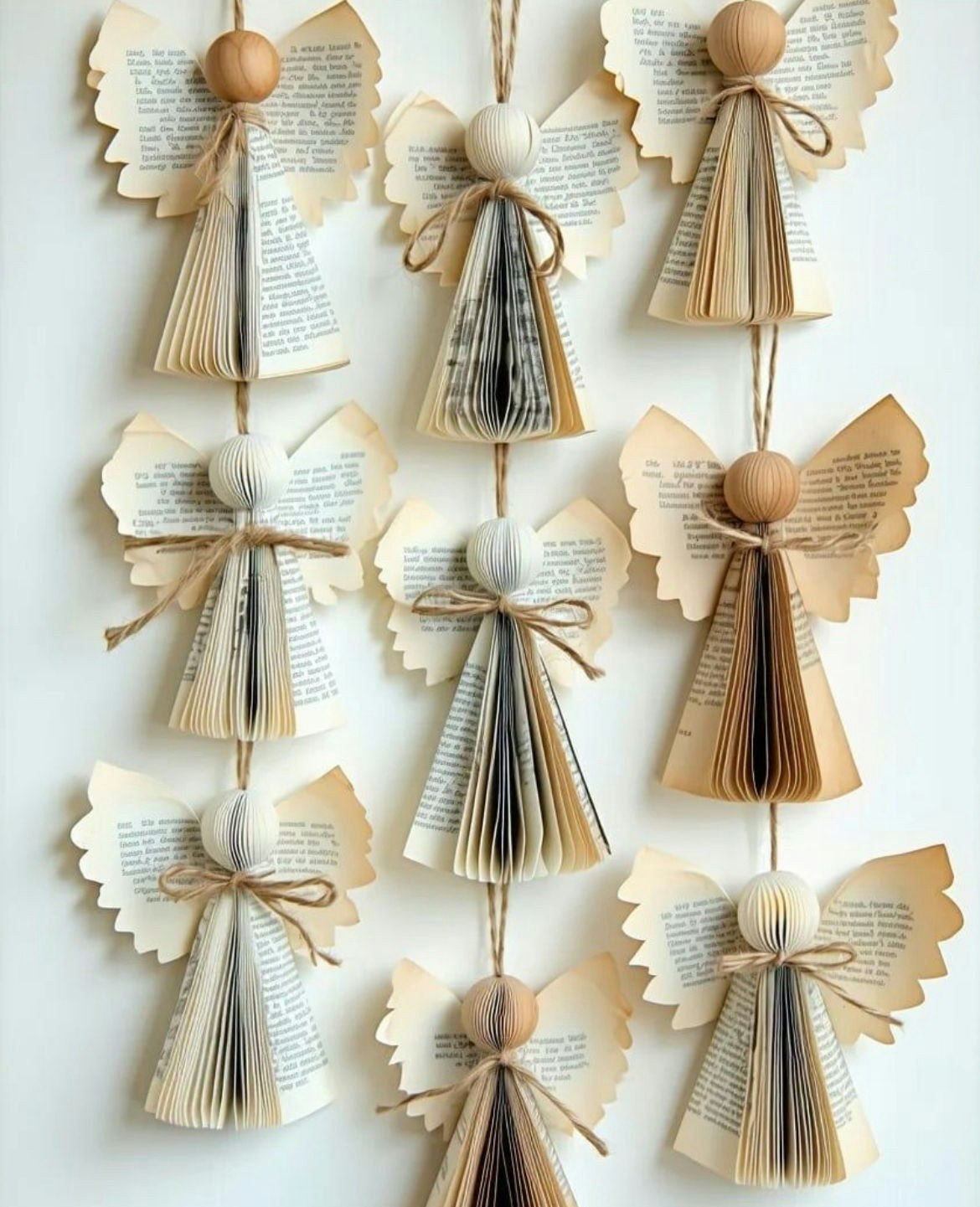 The image features decorative angels made from book pages, featuring round heads and paper wings, hanging on a string.