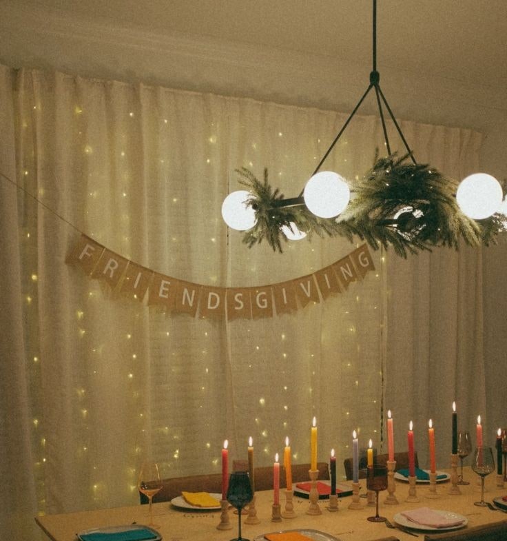 A "Friendsgiving" setup with a decorated table, colorful candles, wine glasses, and a banner under warm lighting.