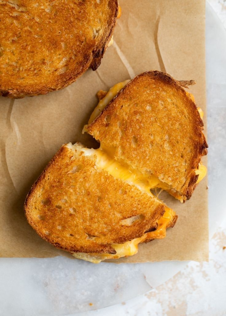 A golden-brown grilled cheese sandwich, cut in half, resting on parchment paper.