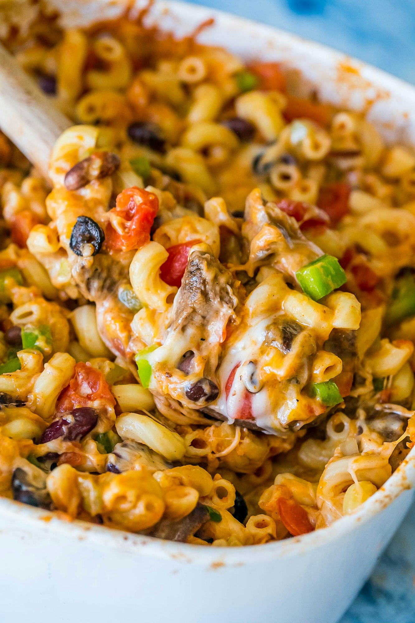 A dish of baked macaroni and cheese with vegetables and beans, showing melted cheese and mixed ingredients.
