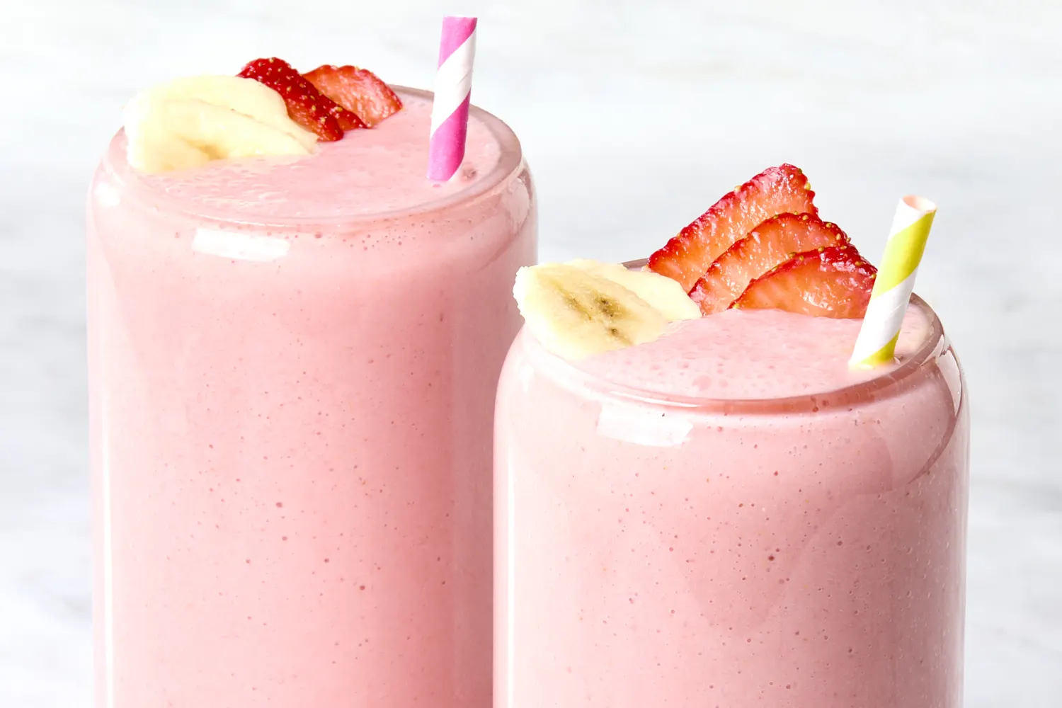 Two pink smoothies with banana and strawberry slices, topped with striped straws.