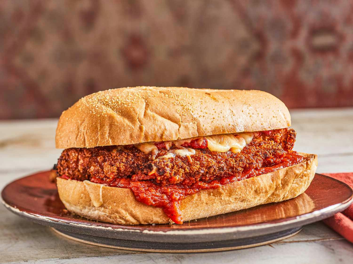 A breaded chicken parmesan sandwich with tomato sauce and melted cheese on a bun.