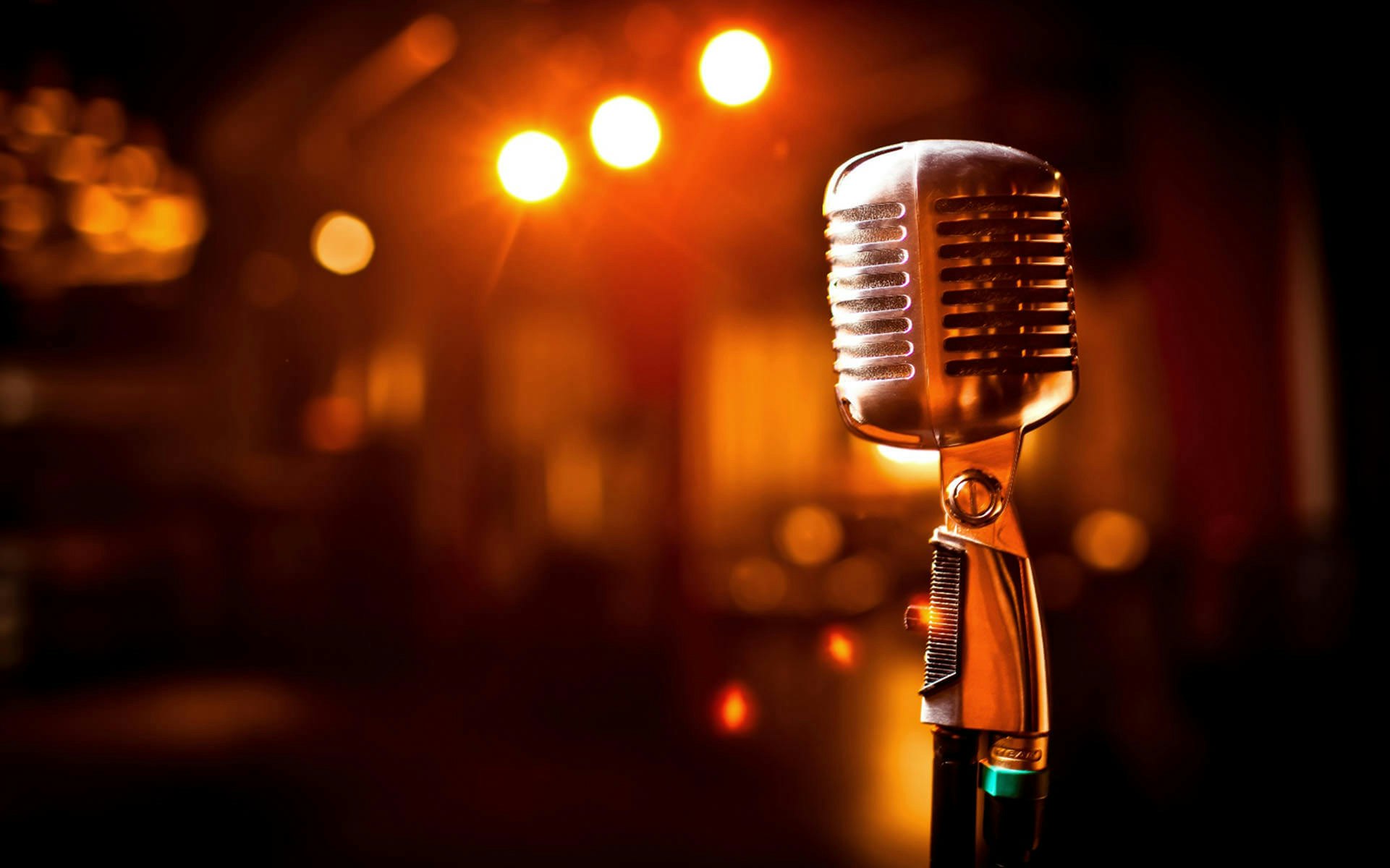 A vintage microphone on a stand with blurred warm stage lights in the background.