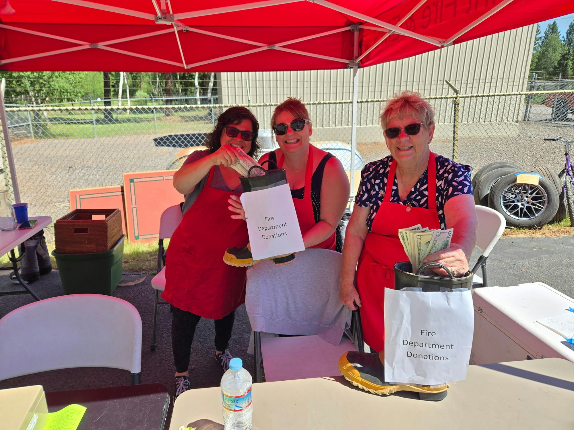 Three people under a red tent collecting donations for the fire department using a boot.