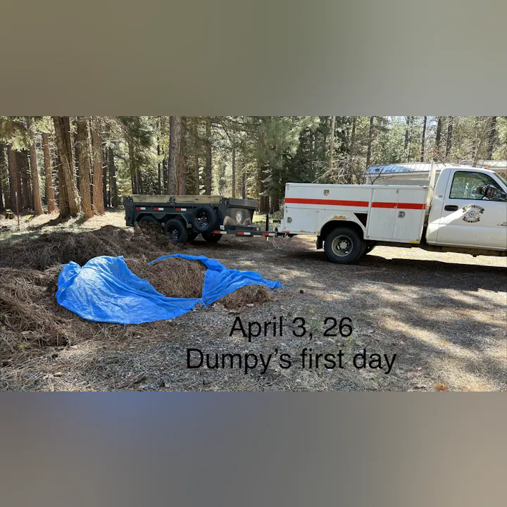 A blue tarp covers some debris in a forest, with a trailer and a service truck nearby. Text mentions "Dumpy's first day."