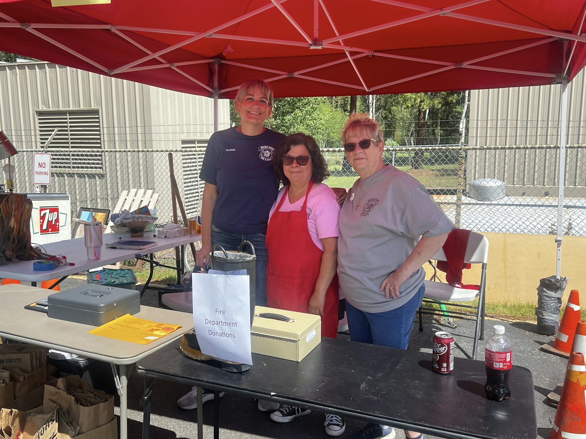 Three people under a red canopy with a donations table for the fire department.
