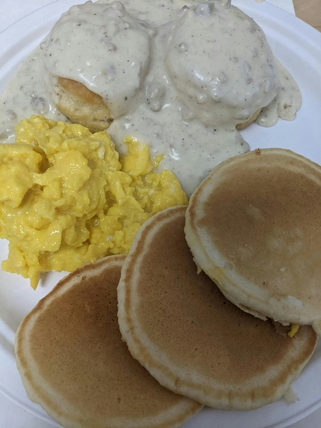 Biscuits with gravy, scrambled eggs, and three pancakes on a plate.
