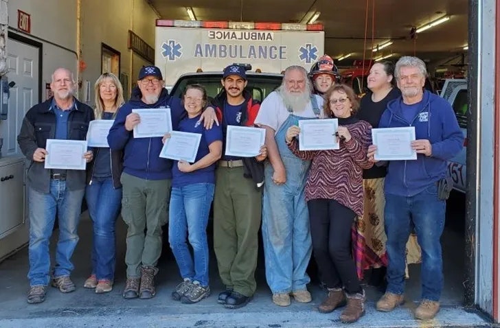 A group of people standing in front of an ambulance, holding certificates and posing for a group photo.