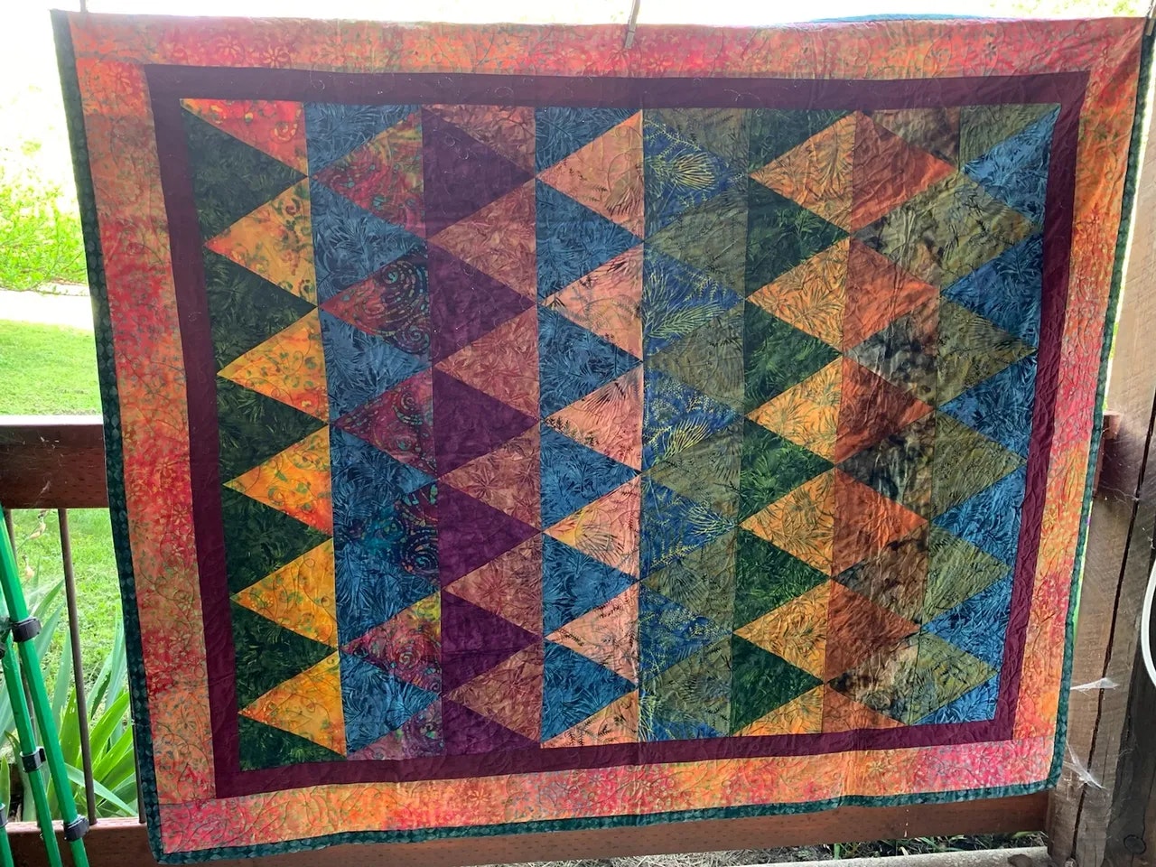 A colorful quilt with a geometric triangle pattern hanging on a porch railing.