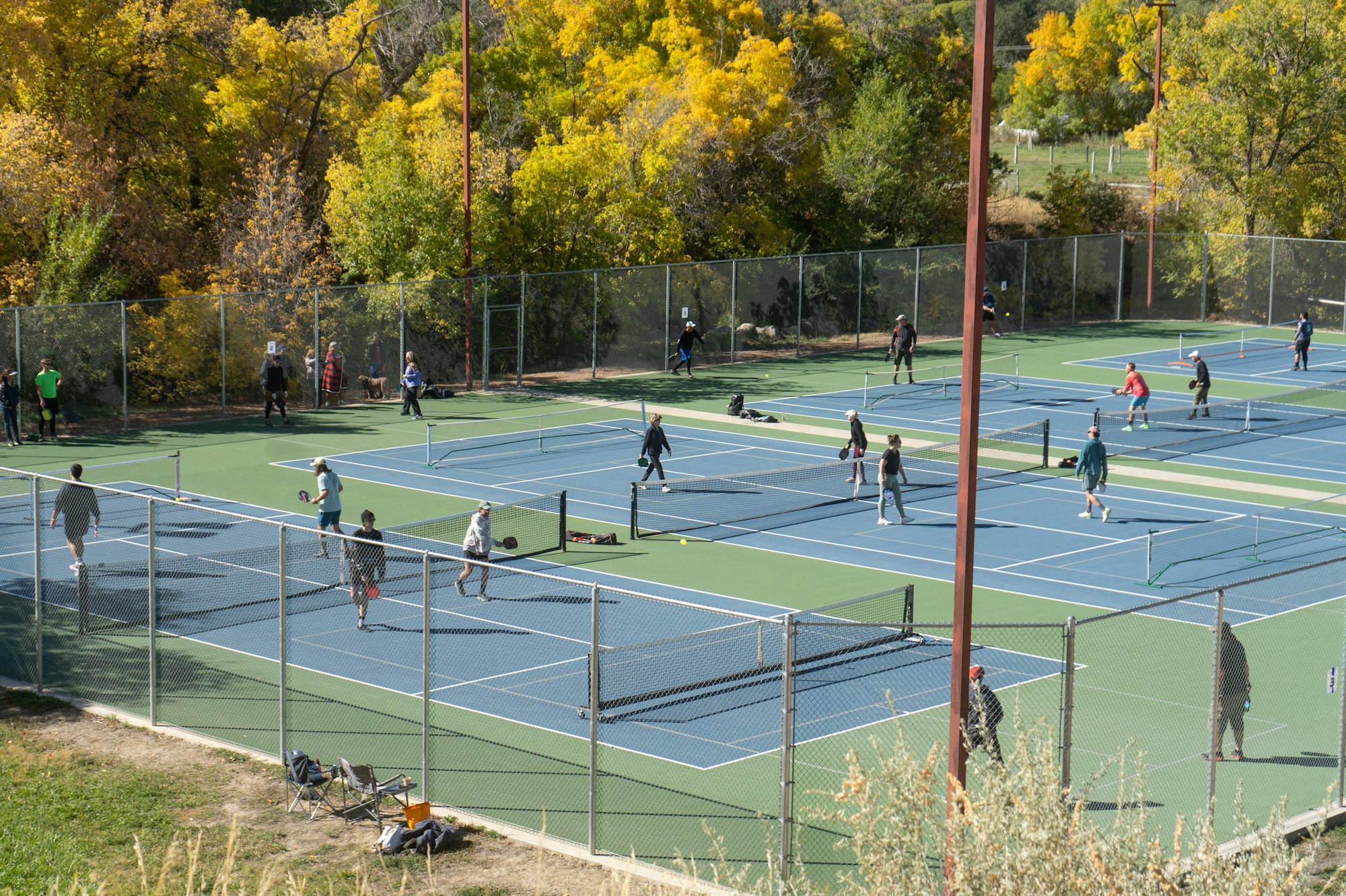 Outdoor tennis courts with players in action, surrounded by trees with autumn foliage.