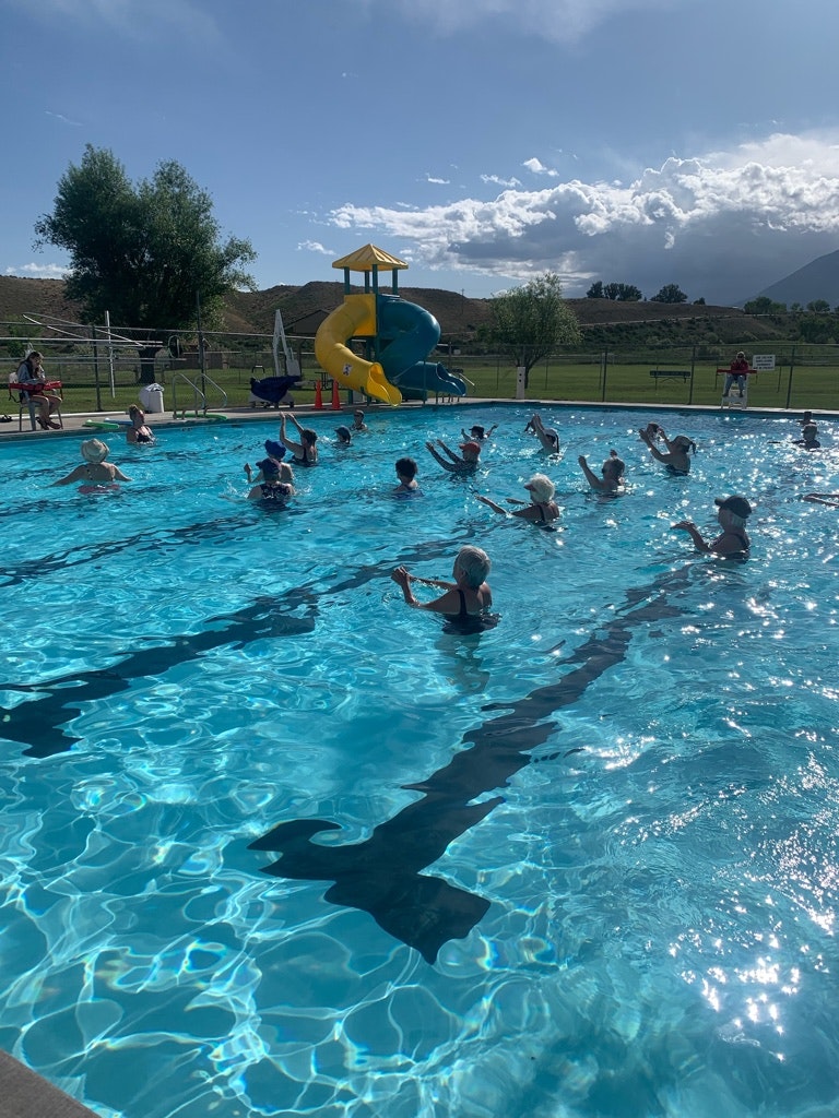 Outdoor swimming pool with people, a slide, sunny sky, and mountain backdrop.